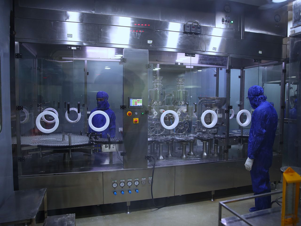 Operators in protective coveralls working at glazed isolator machinery inside a sterile manufacturing area.
