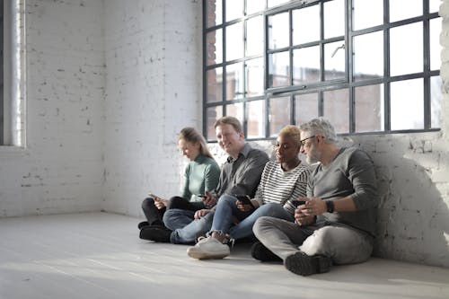 Content multiracial coworkers sitting on floor with smartphones