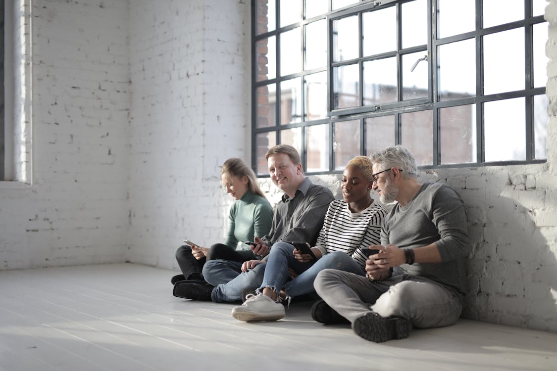 Free Content multiracial coworkers sitting on floor with smartphones Stock Photo