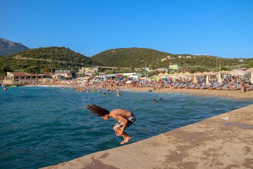Free Man dives into the sea at a crowded beach on a sunny day, showcasing summer fun. Stock Photo