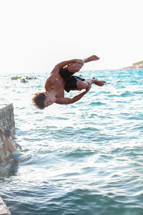 Free A young man performs an acrobatic flip into the ocean on a sunny day. Stock Photo