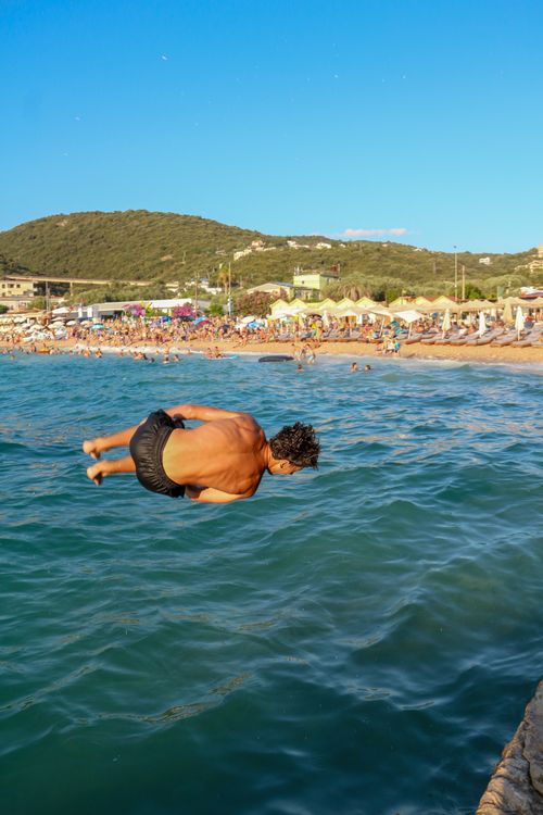 Free A man dives into the ocean off a crowded beach on a sunny summer day, showcasing leisure and excitement. Stock Photo