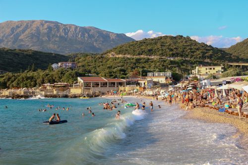 Free Crowded beach with people enjoying a sunny day by the sea, mountains in view. Stock Photo
