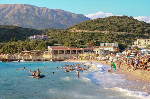 Free Crowds enjoy a sunny day at a bustling Mediterranean beach surrounded by mountains. Stock Photo