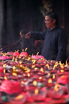 A man carefully lighting candles in a temple, creating a serene, spiritual atmosphere.