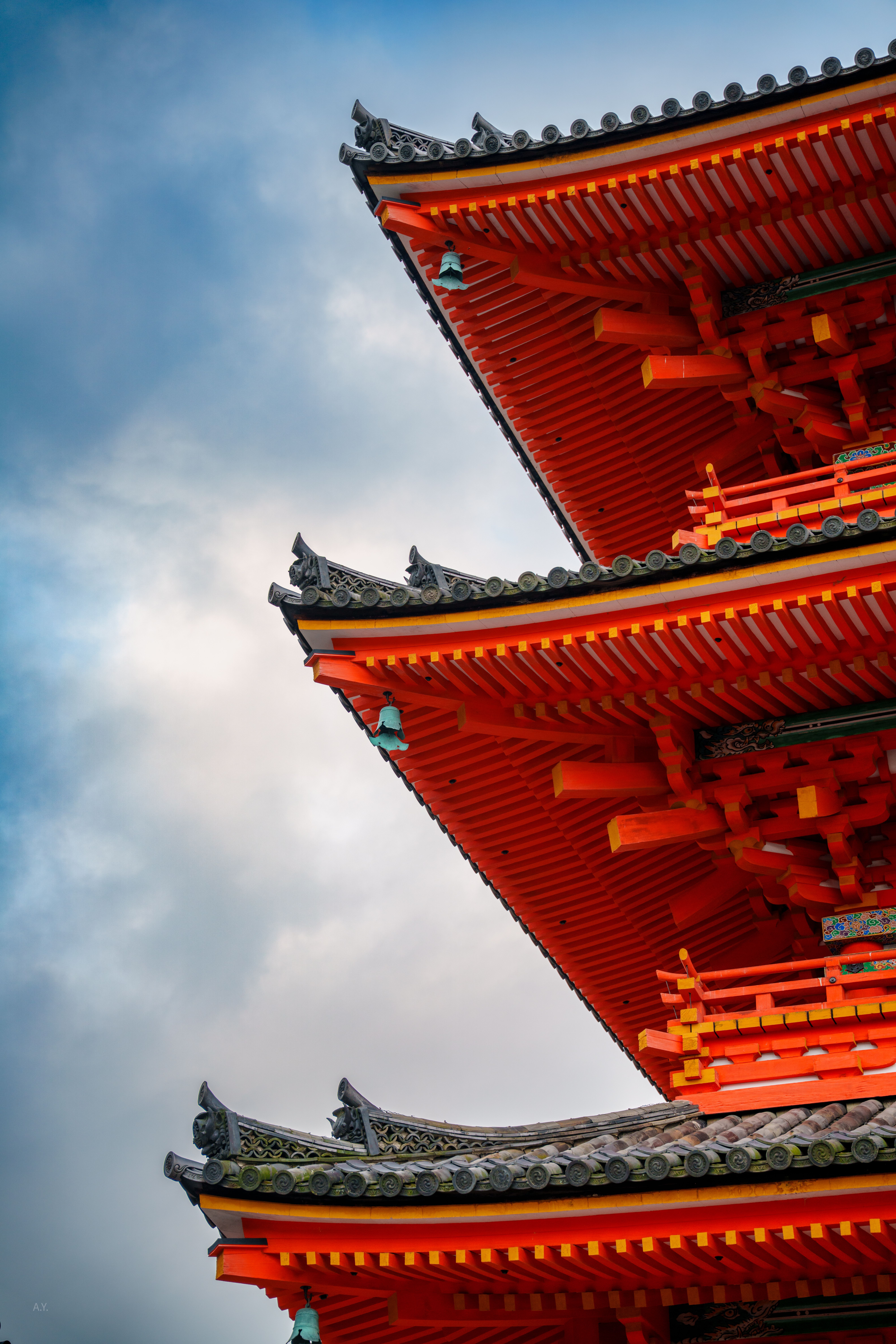 Close-up of a vibrant red traditional Japanese pagoda against a cloudy sky highlighting its intricate details.