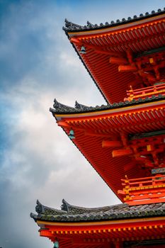 Close-up of a vibrant red traditional Japanese pagoda against a cloudy sky highlighting its intricate details.