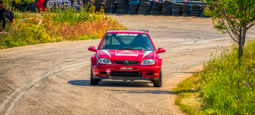 Free A vibrant scene of a red rally car speeding through a winding road during a race in Greece. Stock Photo