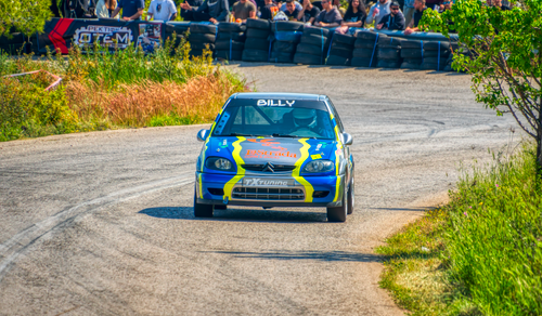 Free Action-packed car race on a winding road with spectators, vibrant rally atmosphere in Greece. Stock Photo