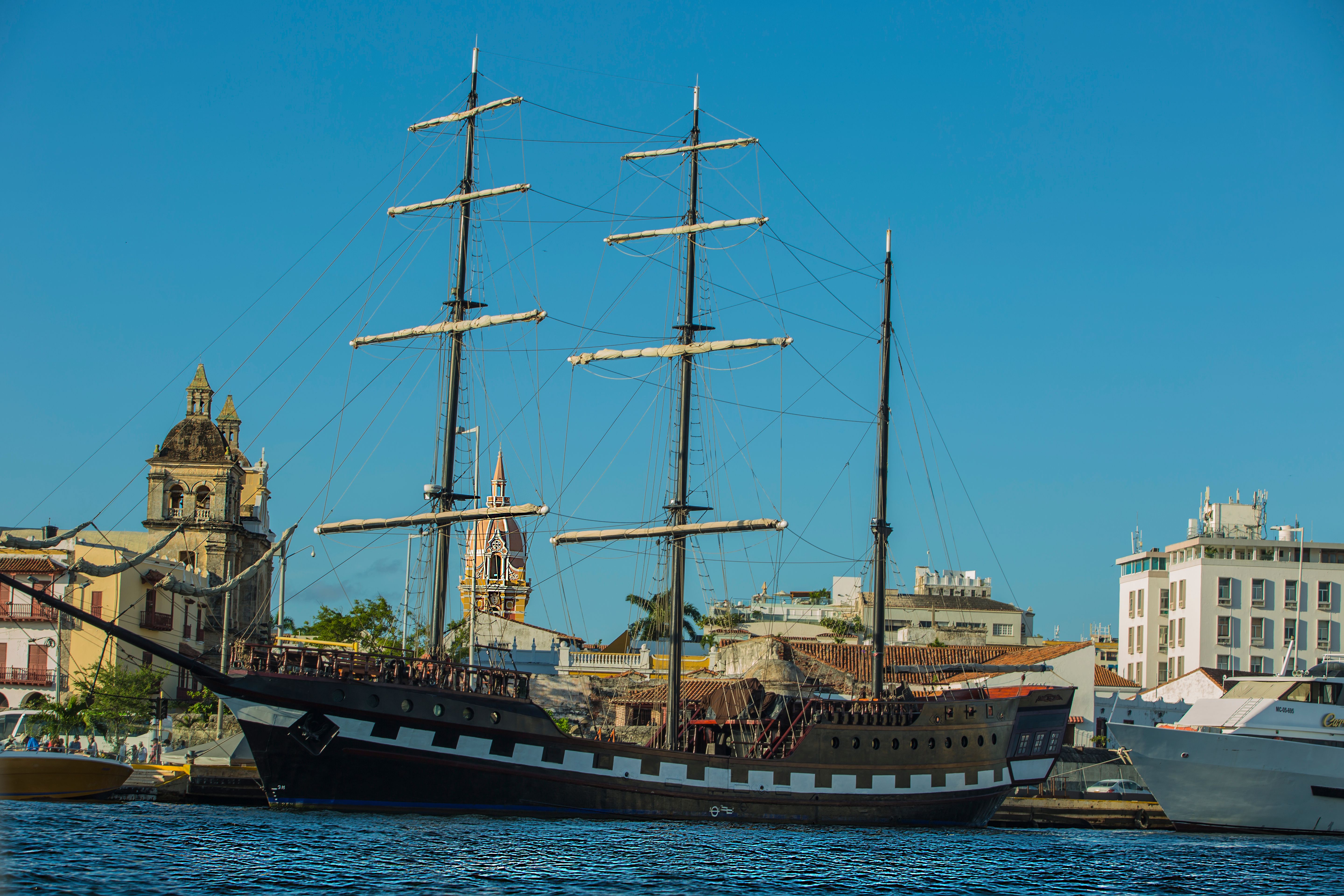 Sailing ship docked in Cartagena with colonial buildings in the background, under a clear blue sky, Colombia
