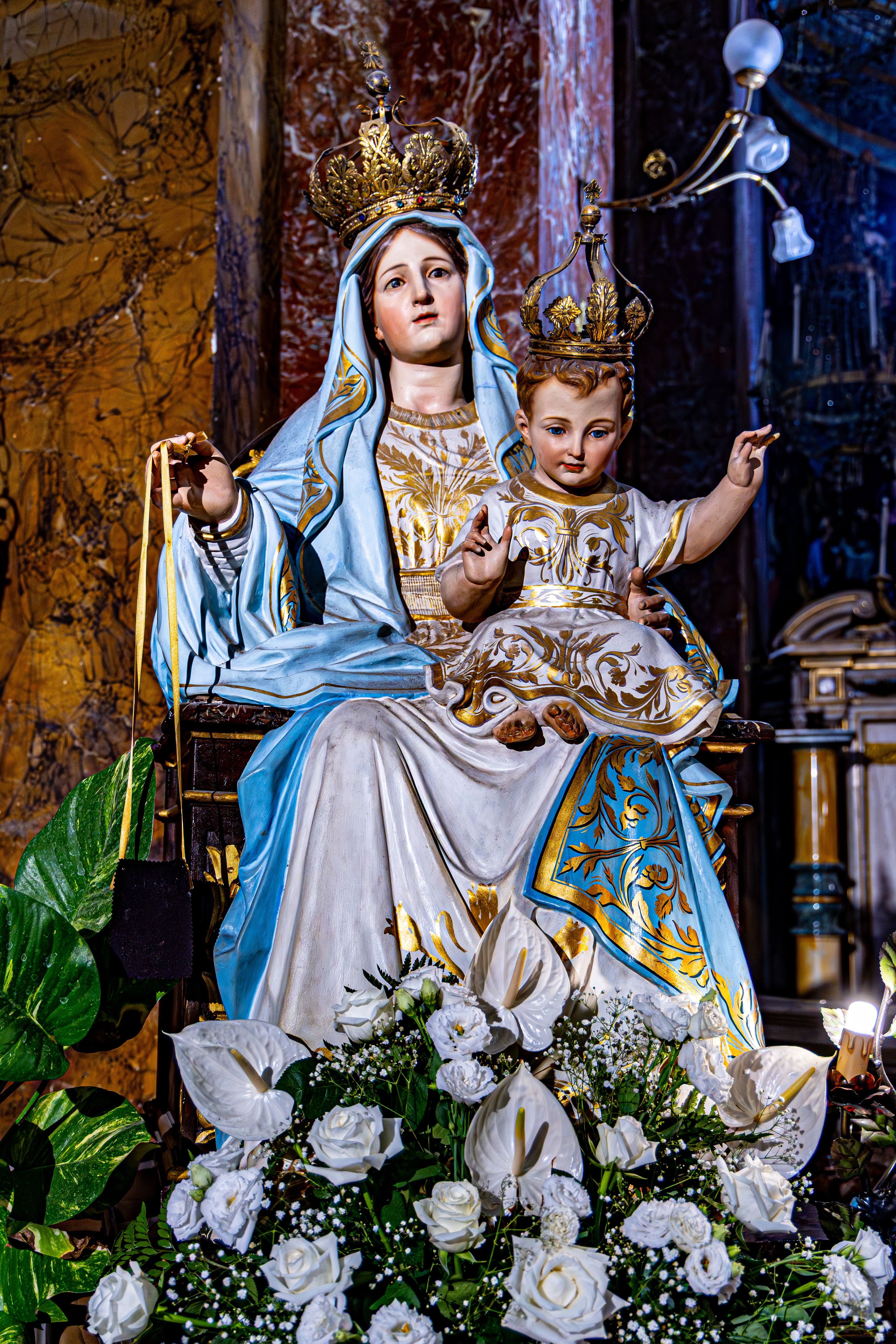 A detailed statue of Mary and child in a church setting with floral decor.