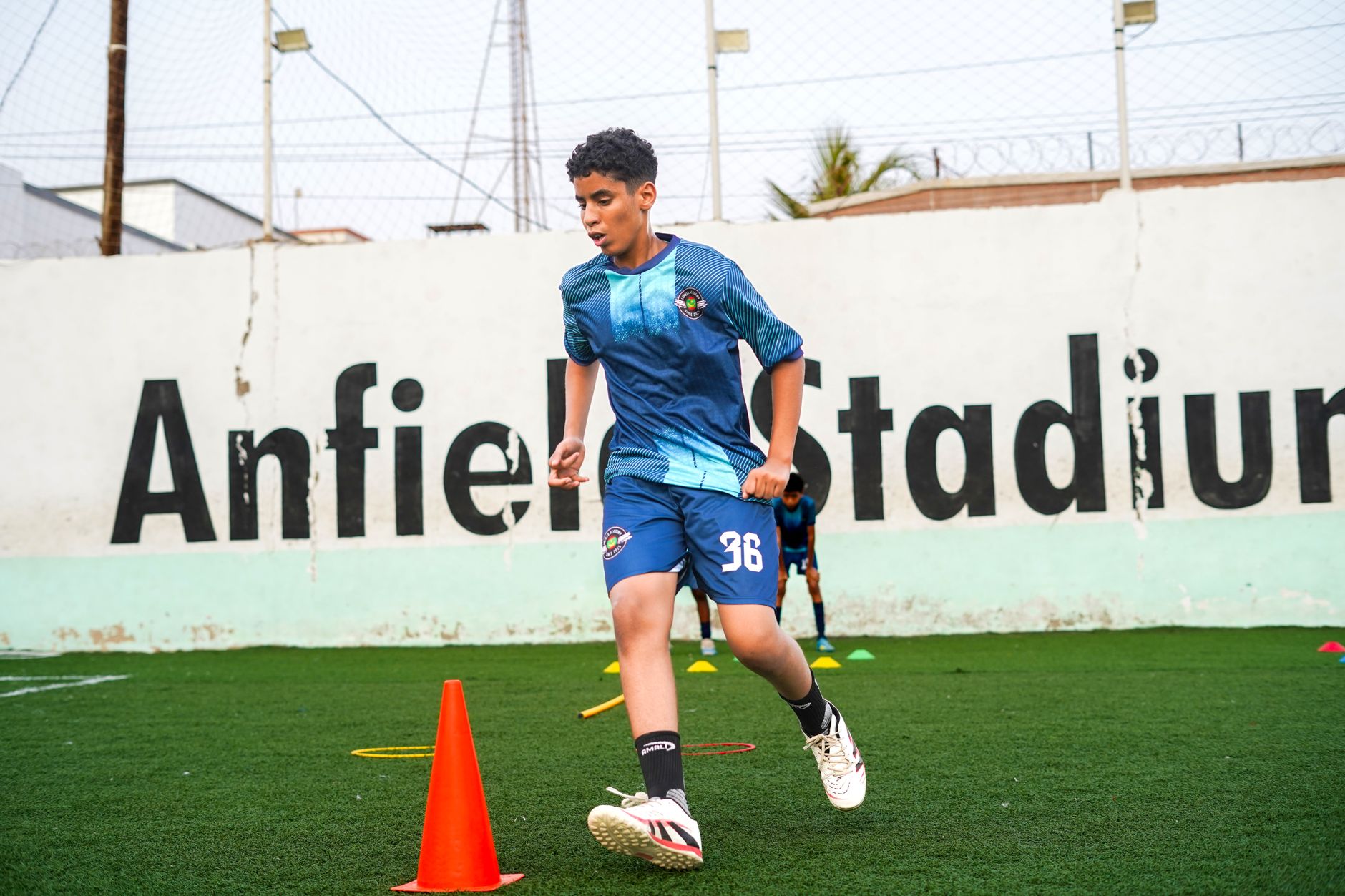 A coach timing a football agility drill while a player changes direction through flat yellow markers