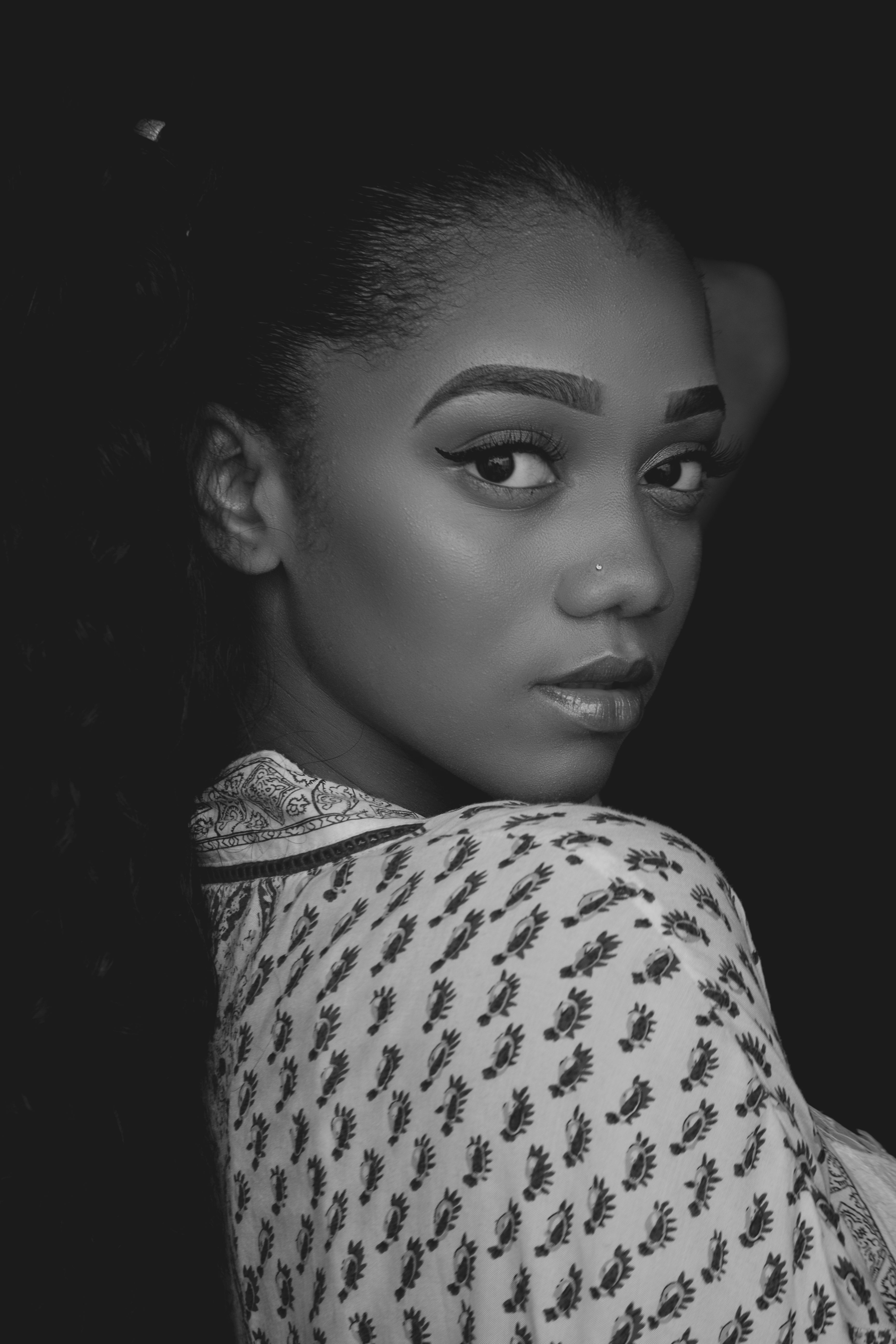 A striking black and white portrait of a woman with a confident gaze and intricate patterned clothing.