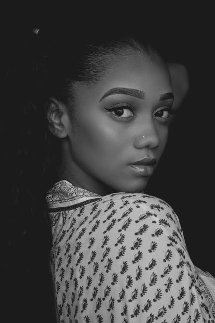 A striking black and white portrait of a woman with a confident gaze and intricate patterned clothing.