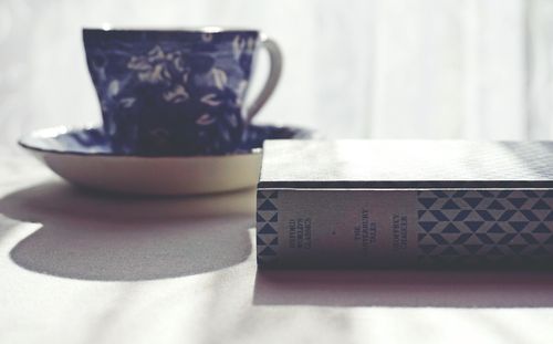 Free A vintage blue tea cup and a classic book on a white tablecloth, lit softly. Stock Photo