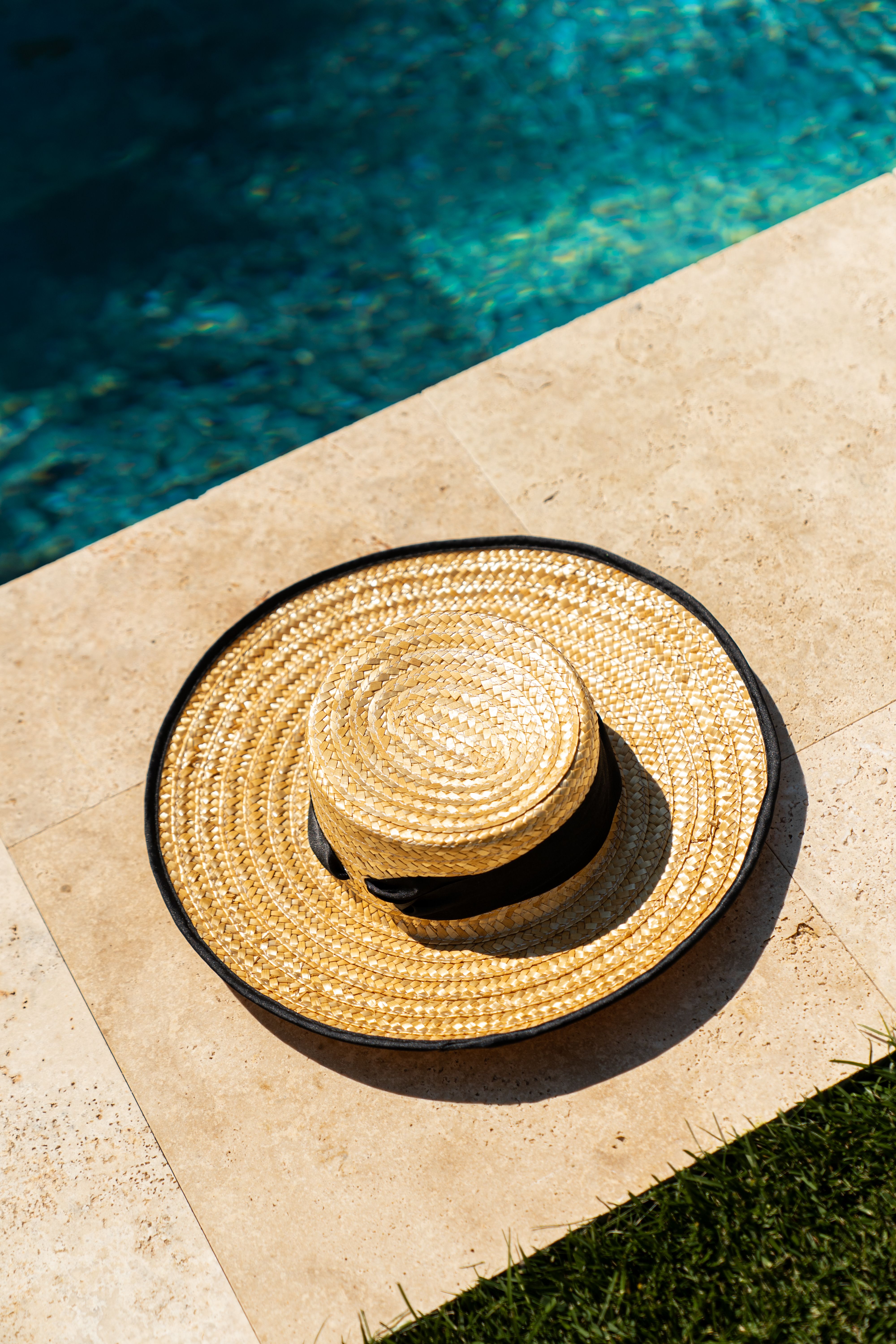 A straw hat rests by a clear blue pool, suggesting a relaxing summer day.