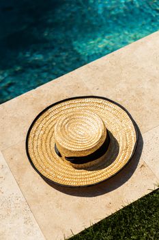 A straw hat rests by a clear blue pool, suggesting a relaxing summer day.