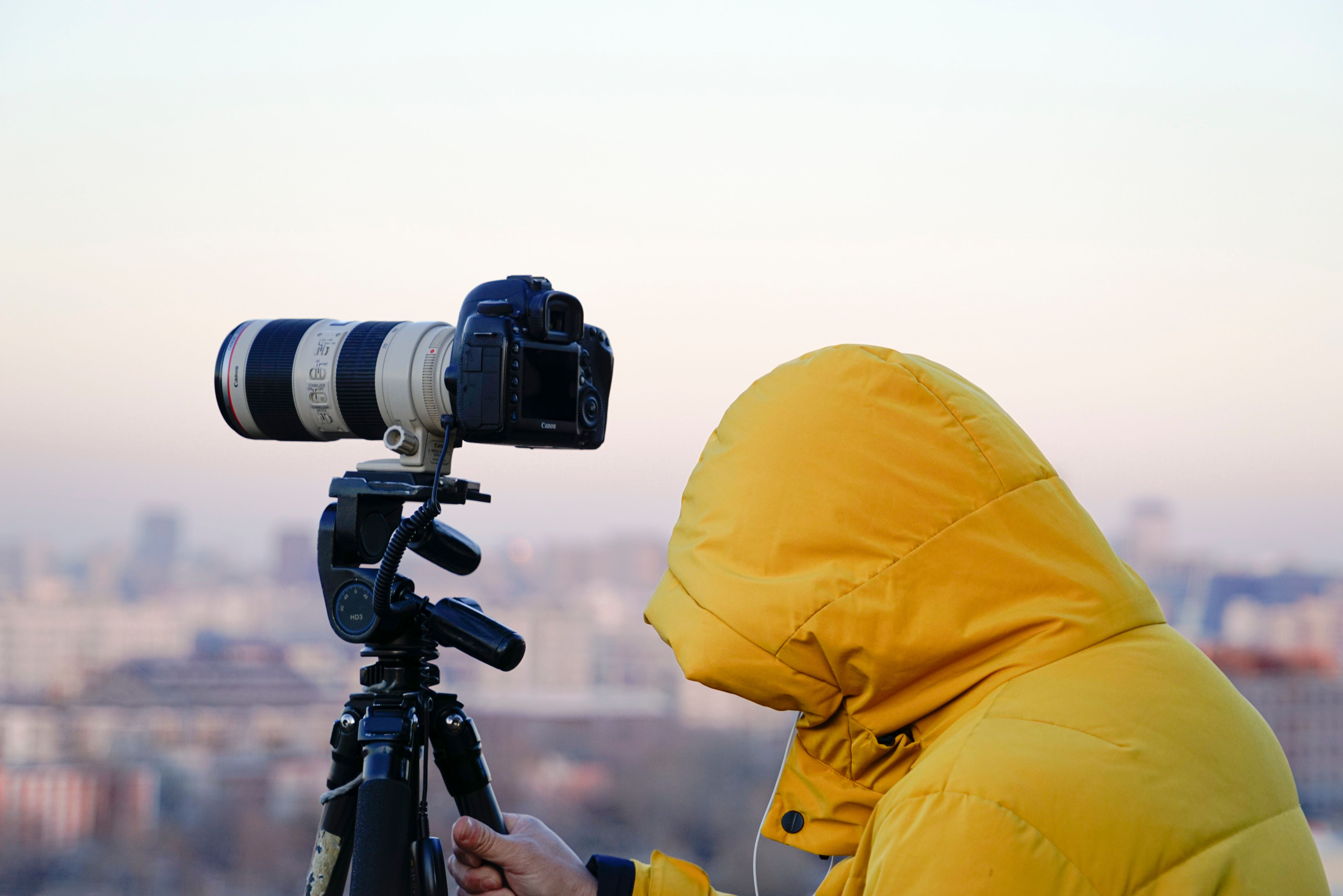 A photographer in a yellow jacket using a DSLR on a tripod to capture a cityscape in Beijing.
