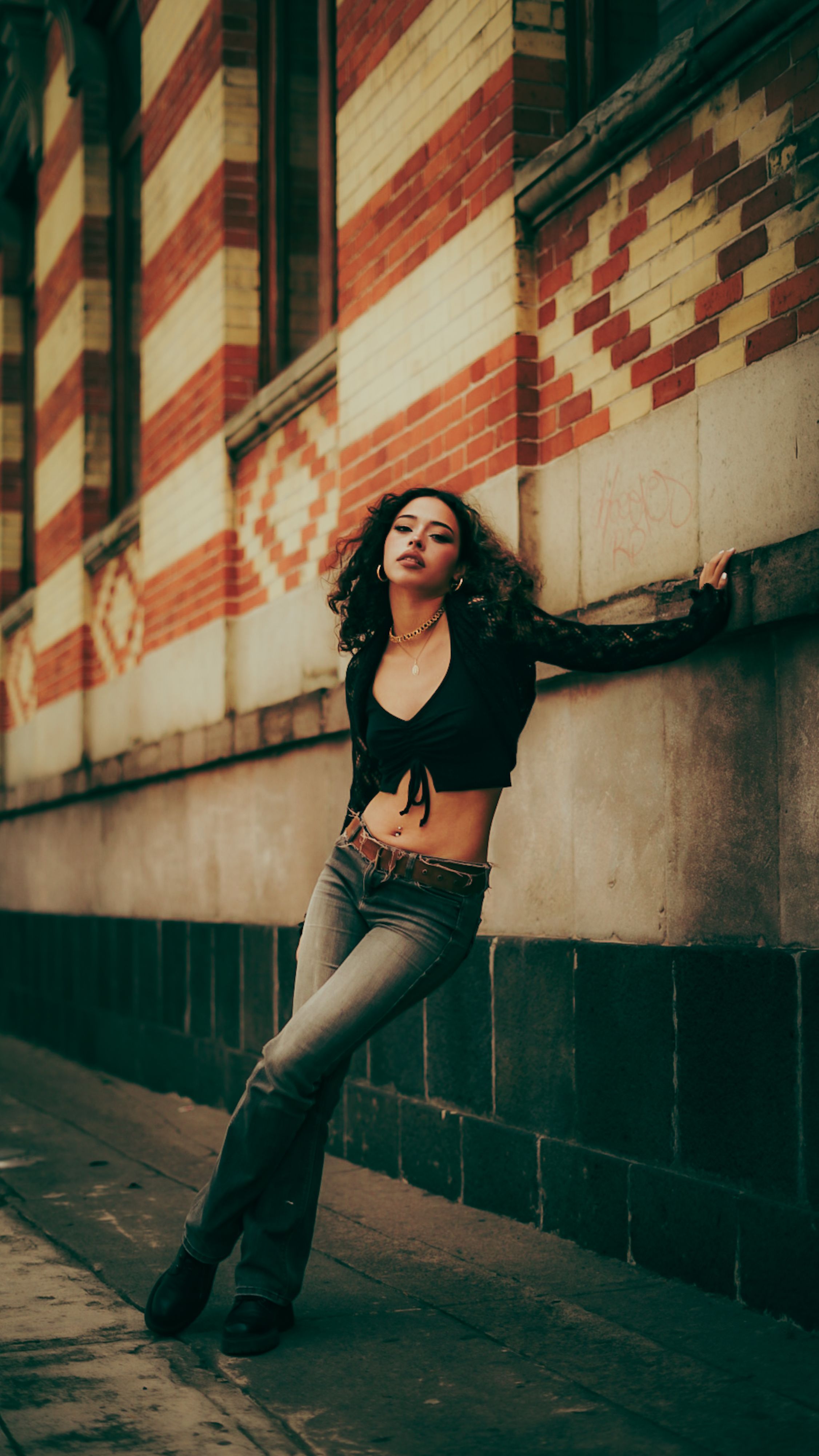 Fashionable young woman standing against a vibrant brick wall in a city setting, exuding confidence and style.