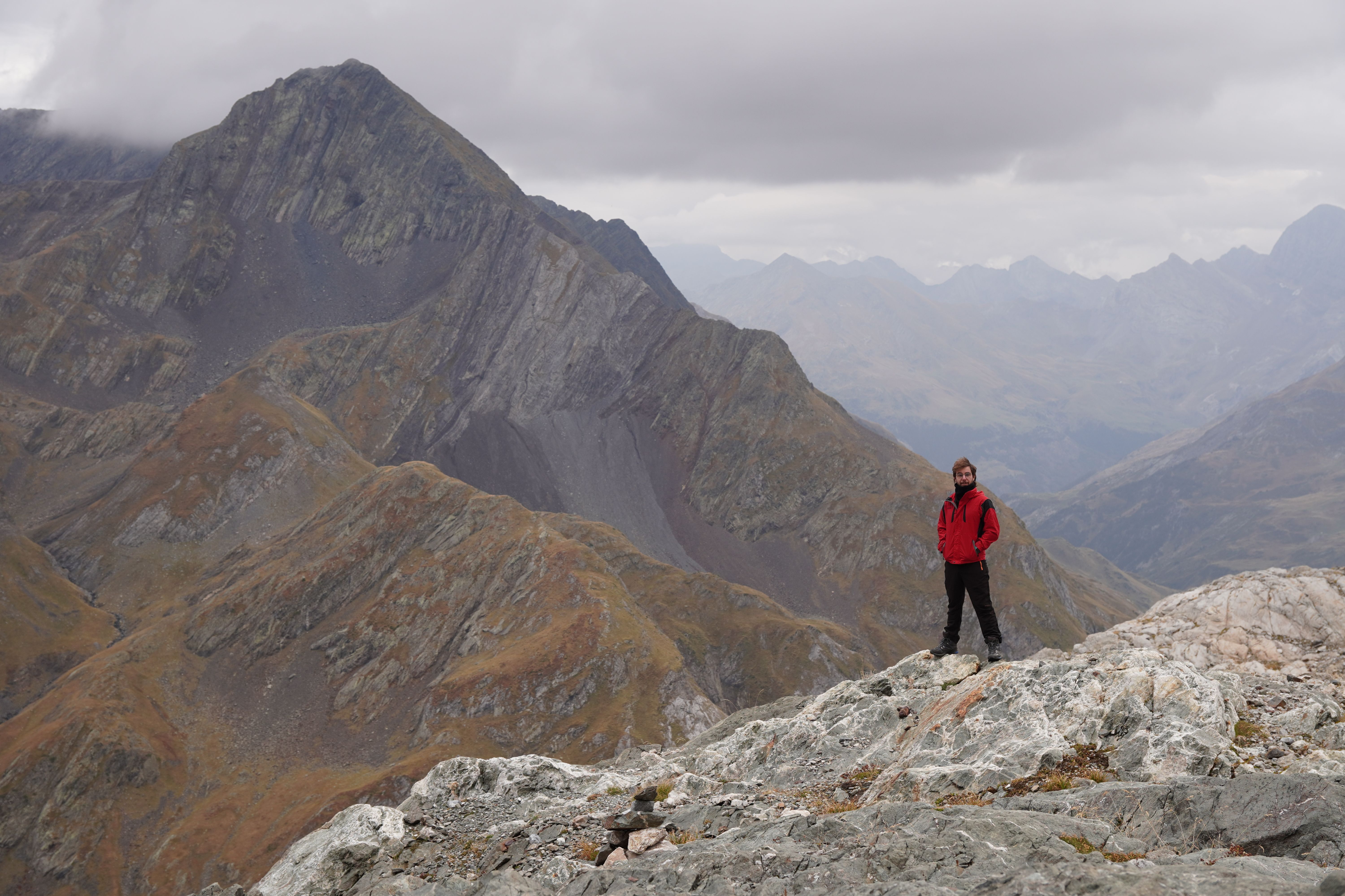 An adventurer in a red jacket stands atop a rocky mountain, surrounded by dramatic peaks.