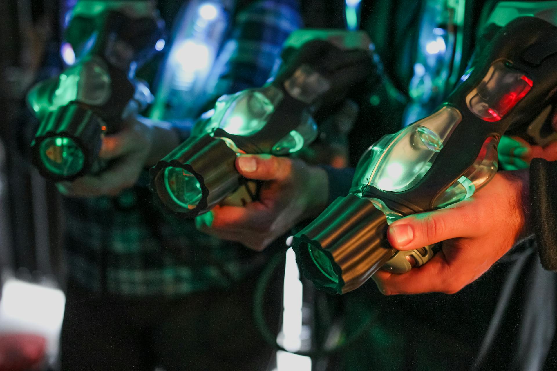 Close-up of players holding illuminated laser tag guns indoors.