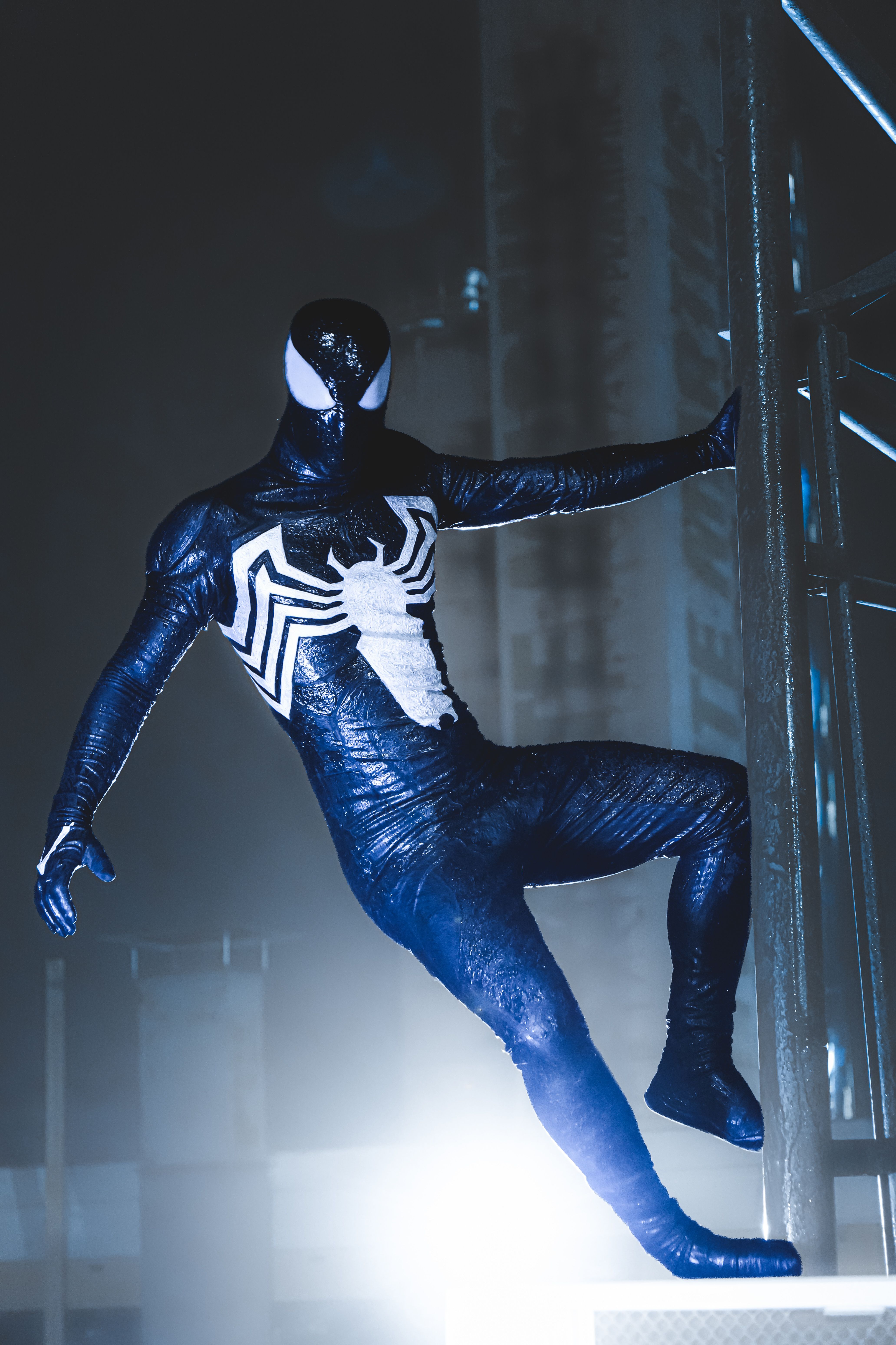 Dynamic image of a costumed hero in a black and white suit, hanging from a metal framework.