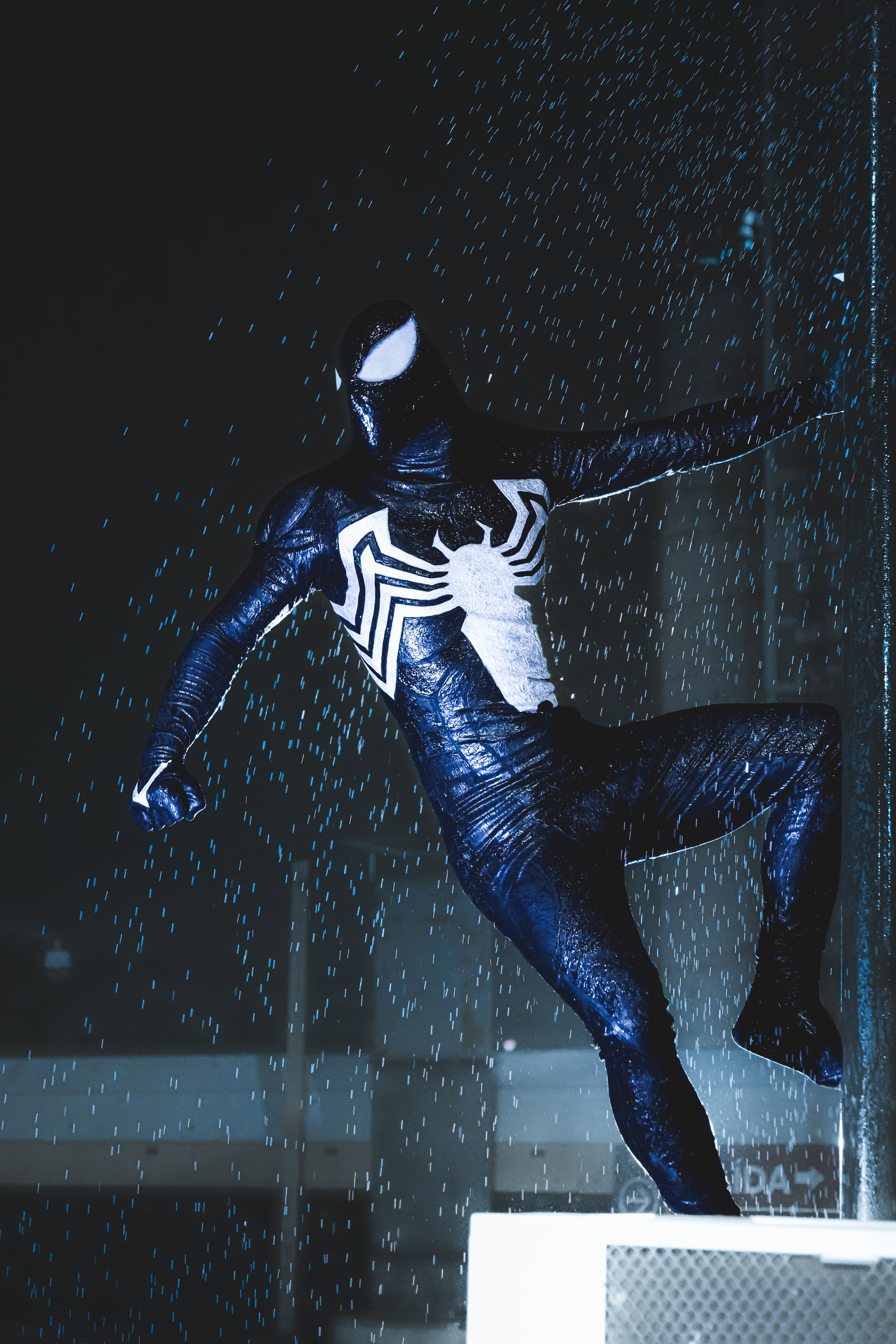 Dynamic shot of a superhero in a black suit amid raindrops at night.