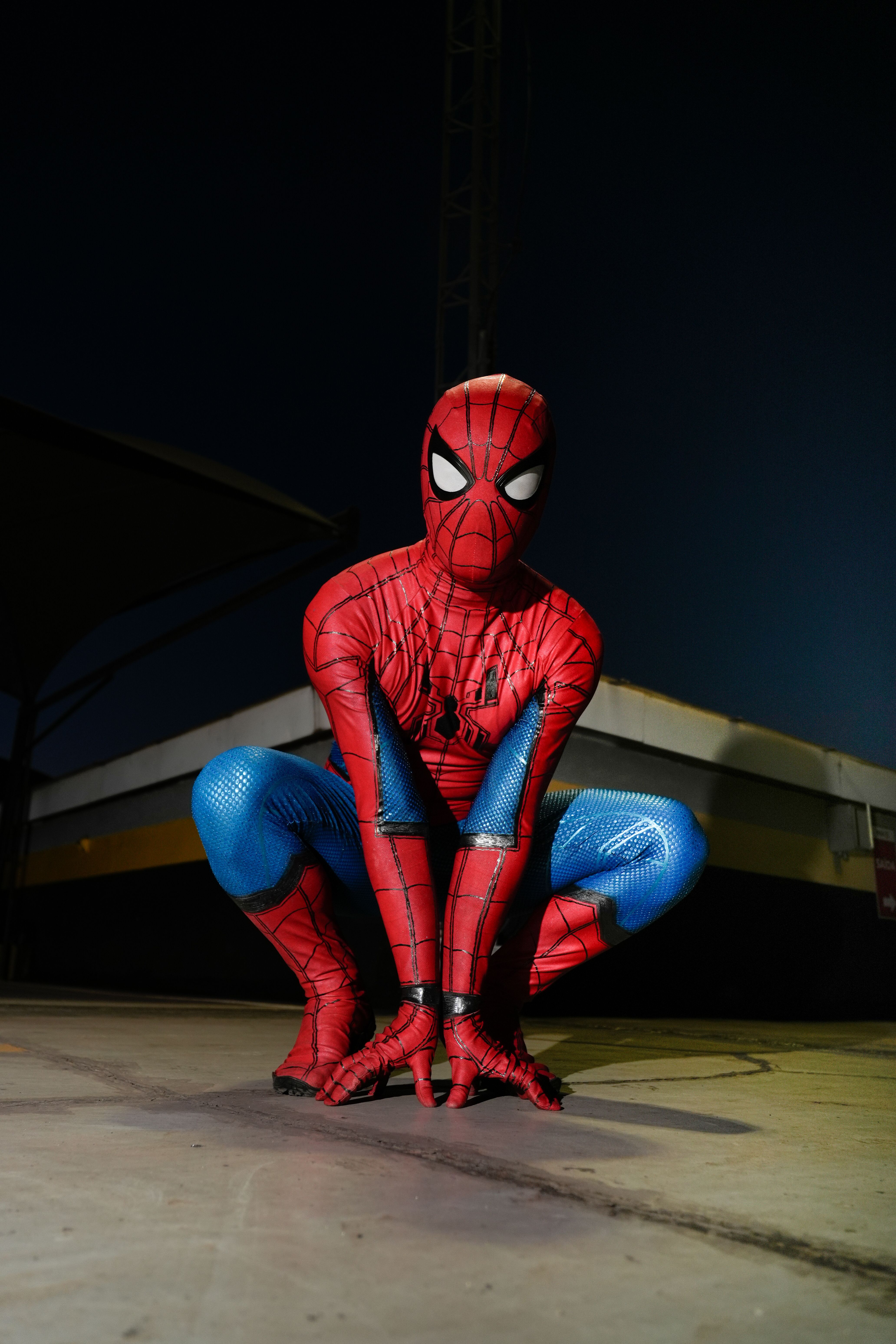 A person in Spider-Man costume crouching outdoors at night, poised for action.