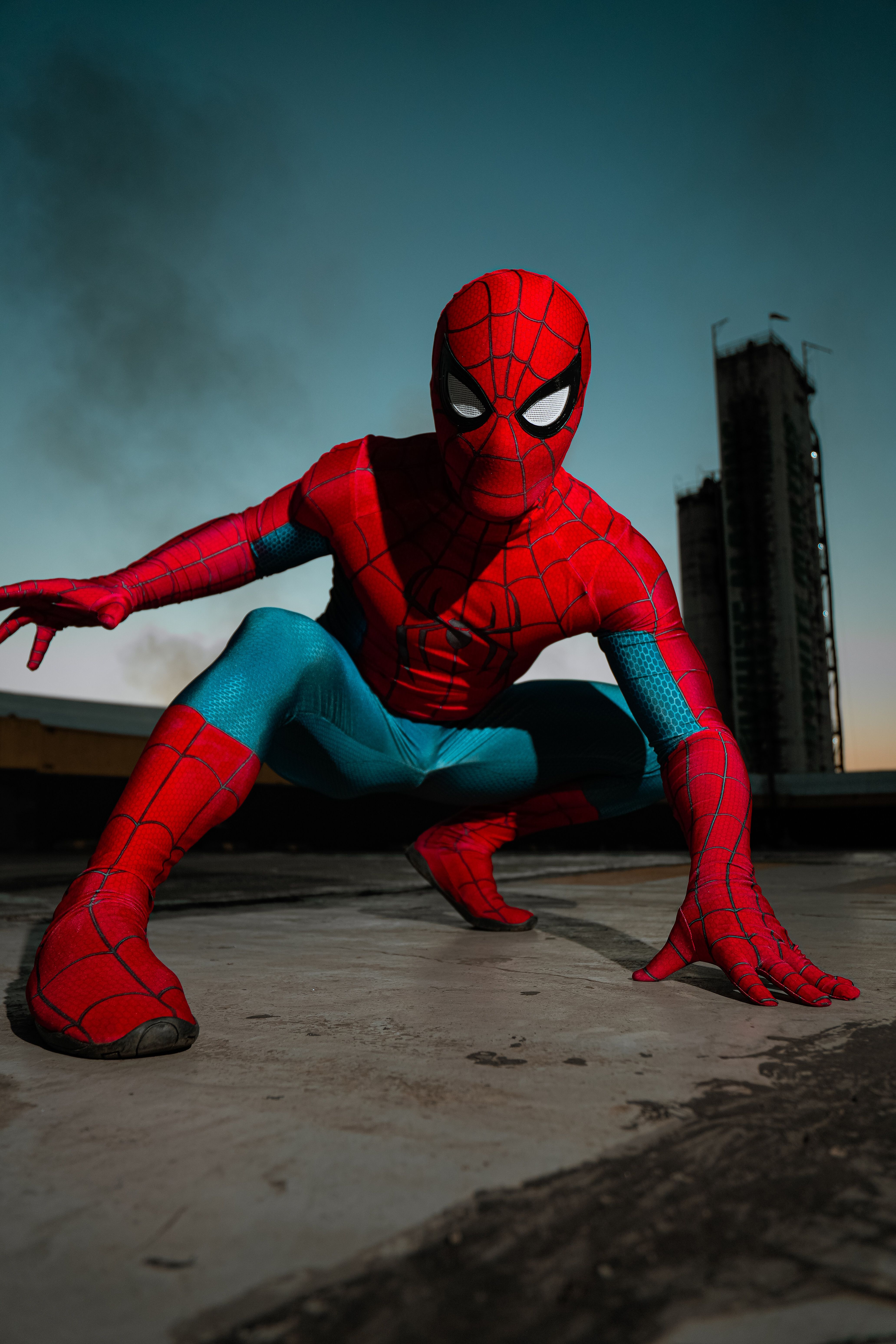 A costumed superhero poses dramatically on a rooftop at dusk.