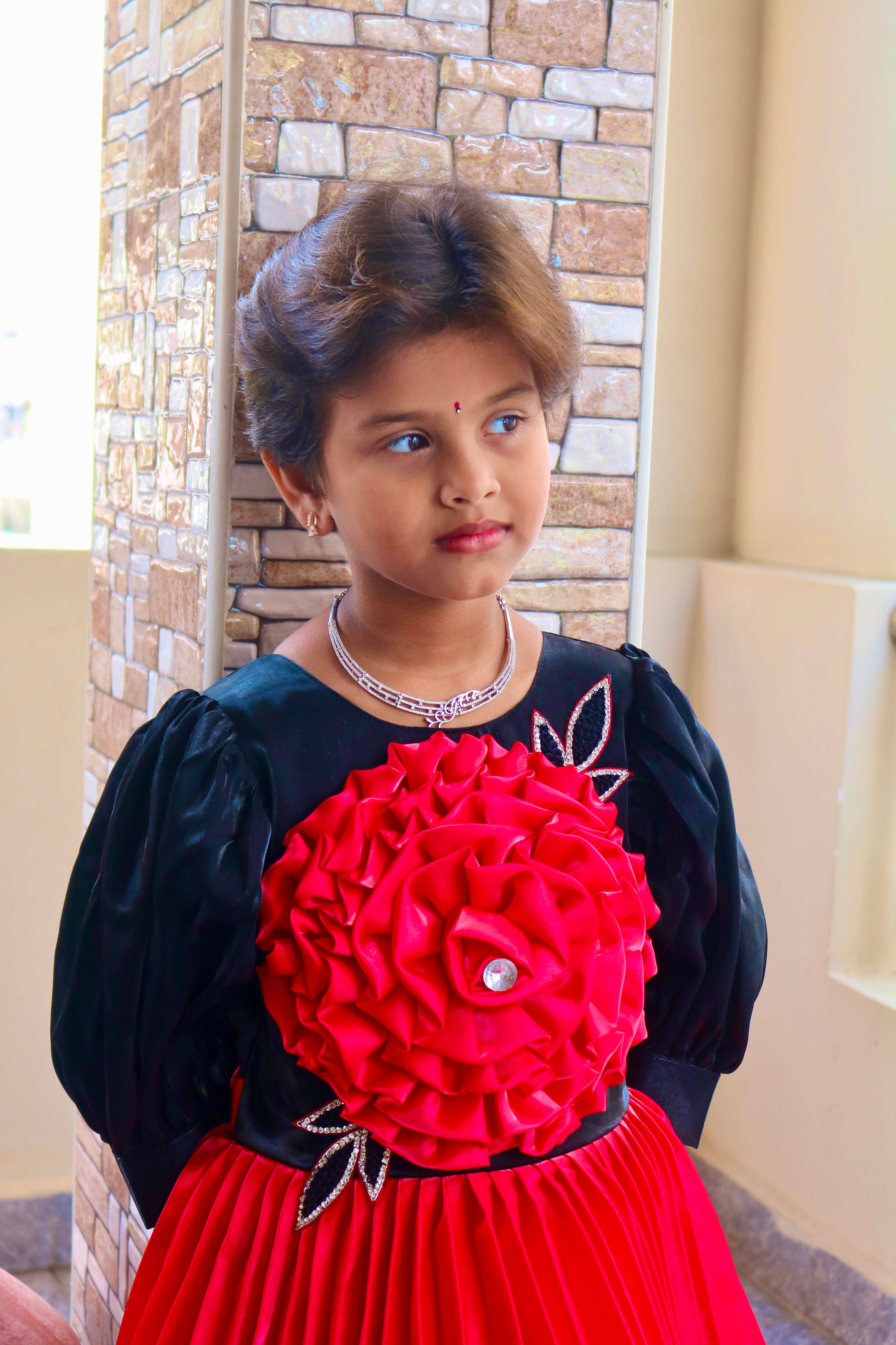 Adorable young girl in a black and red floral dress posing indoors, exuding elegance and charm.