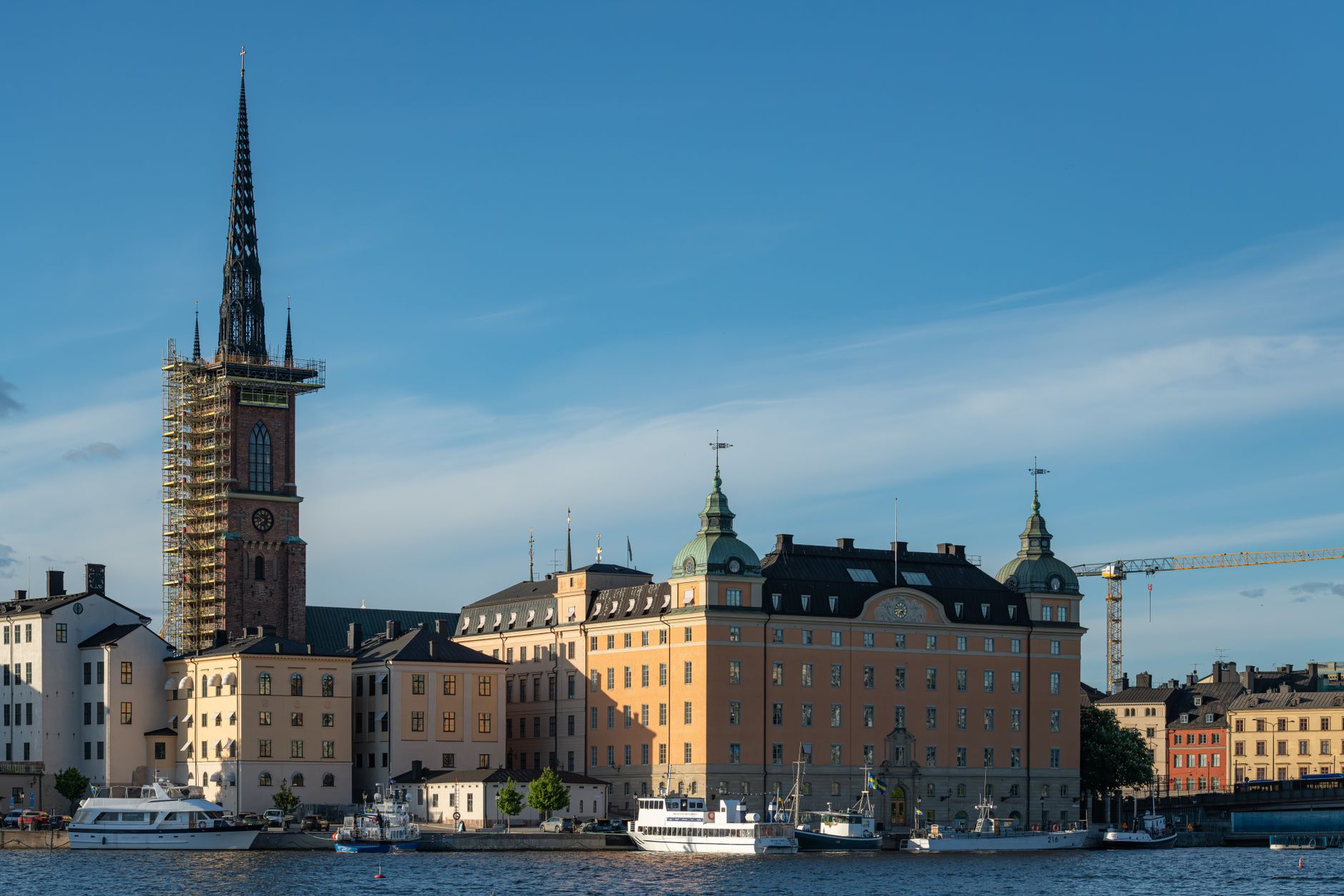 Scenic view of Riddarholmen Church next to a waterfront in Stockholm under a clear blue sky.