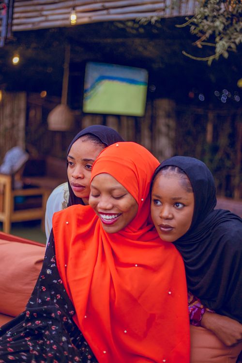 Free Smiling friends in vibrant hijabs share a joyful moment in a cozy cafe setting. Stock Photo