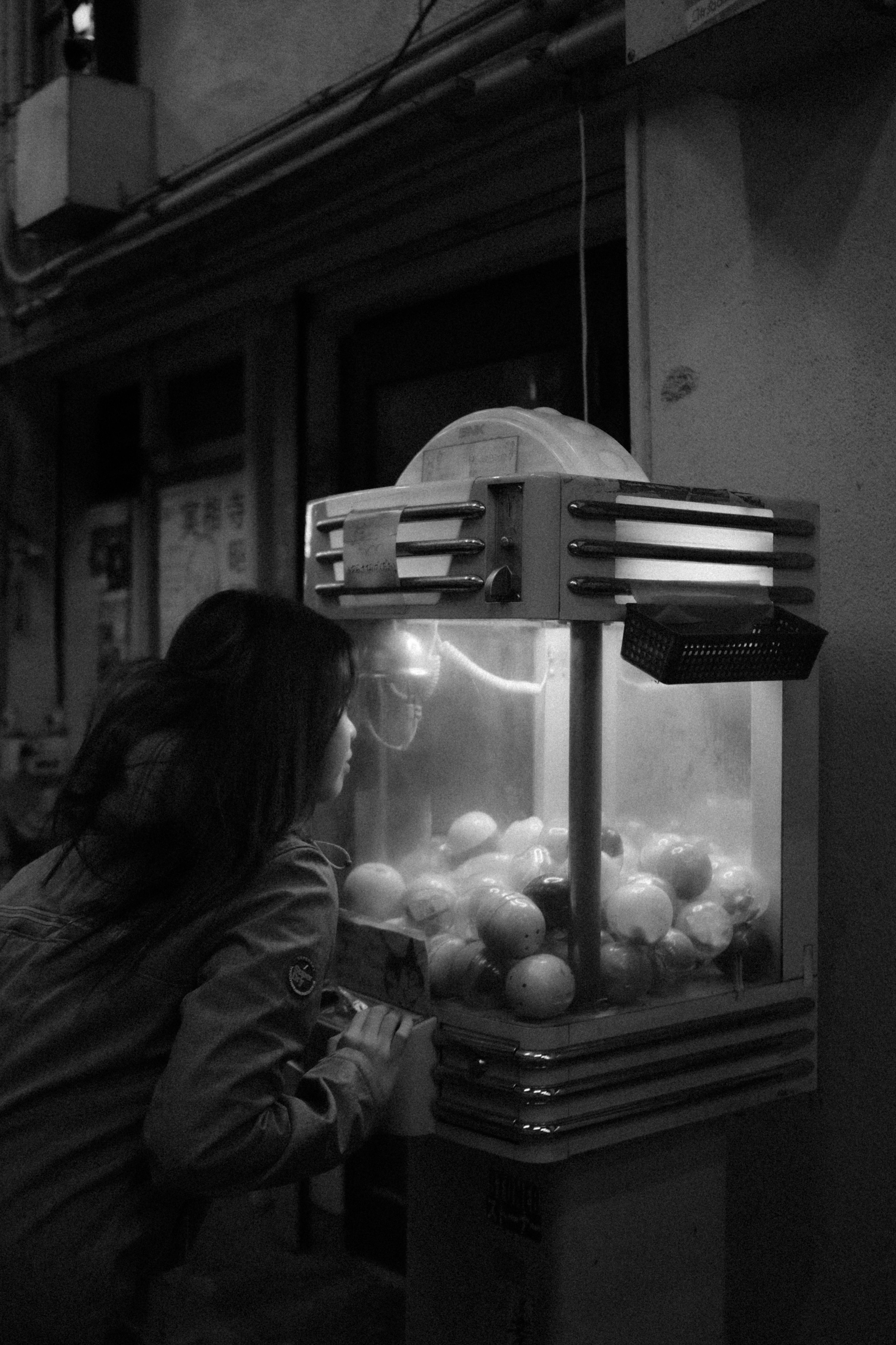 Black and white photo of a woman at a Gacha machine in Japan at night.