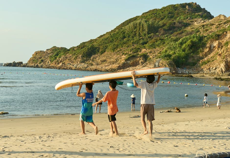 Group of children carrying a surfboard on a sunny day at Quy Nhon beach in Vietnam.