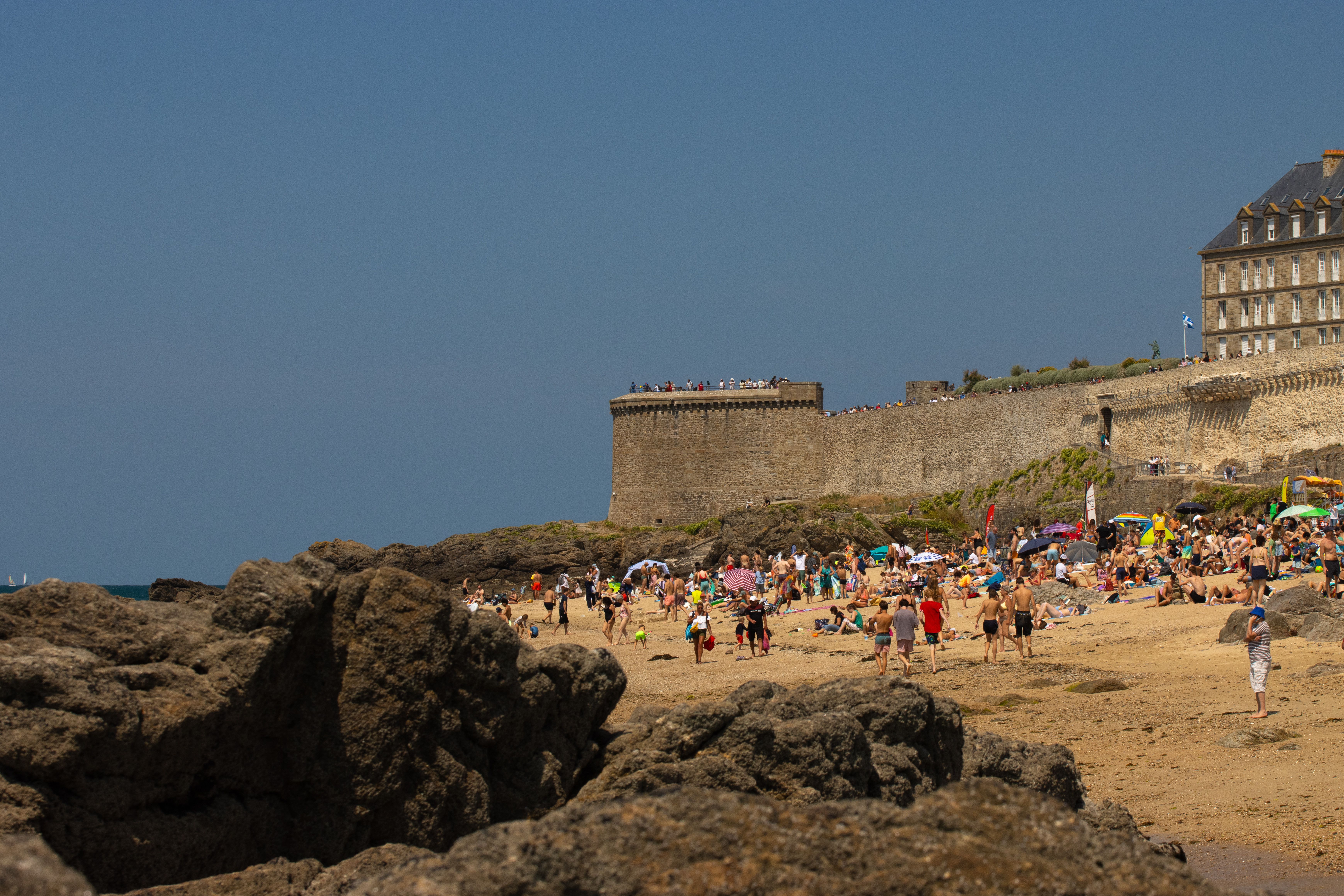 Sunny beach with a historic stone wall in the background under a clear sky.