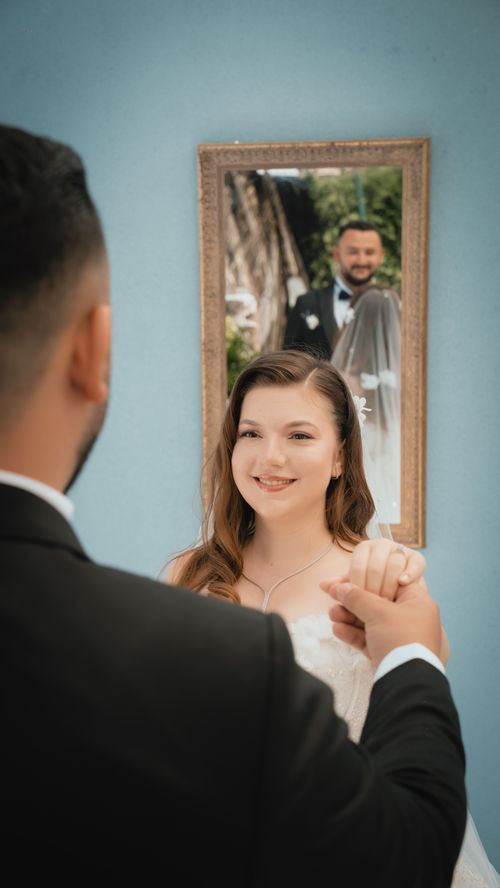 Free A bride smiles into a mirror while holding hands, reflecting her groom's image in a loving setting. Stock Photo