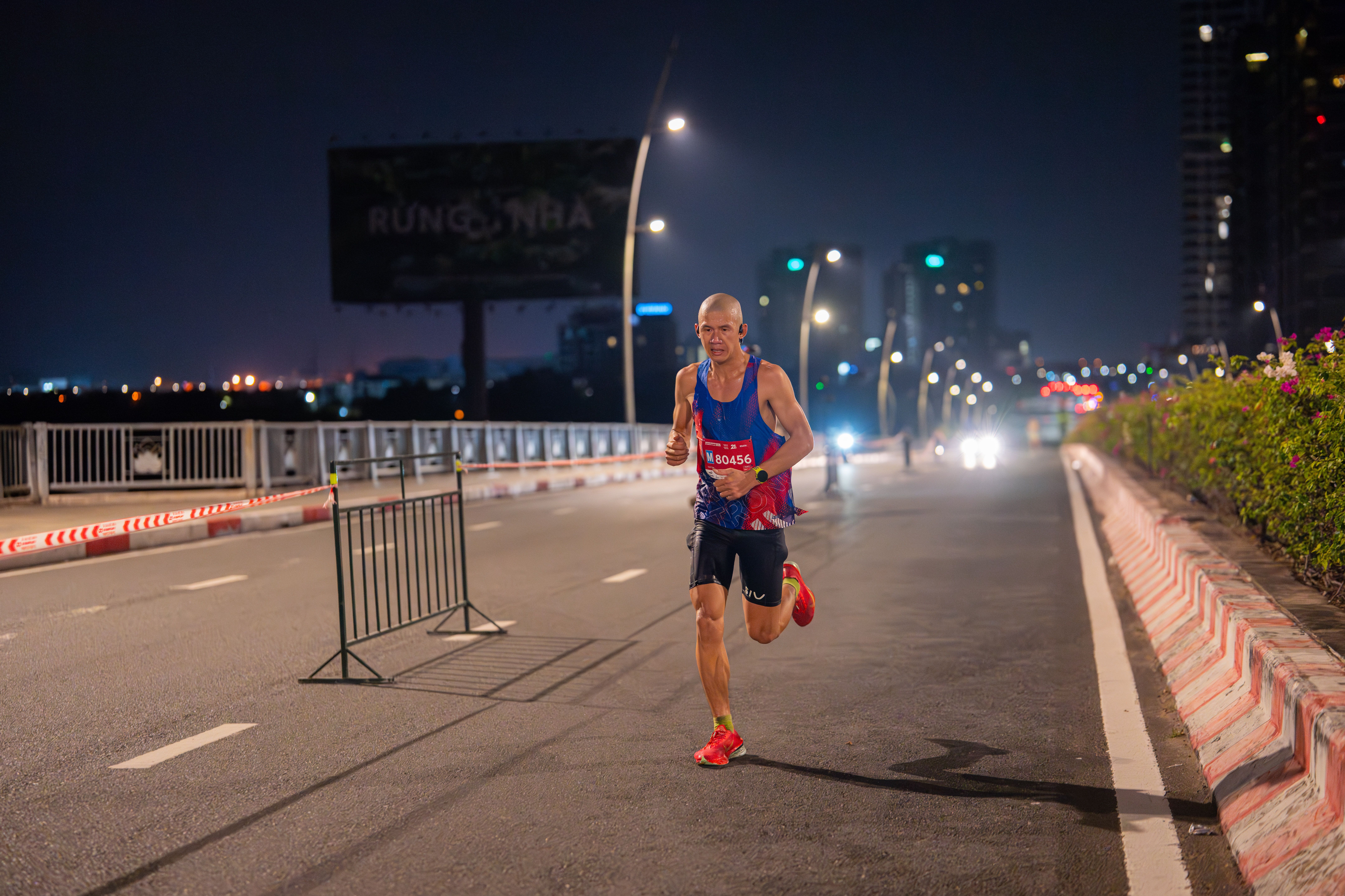 A focused runner competes in an urban marathon at night, road illuminated by streetlights.