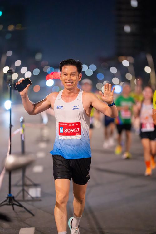 Free Runner with bib M80957 smiles and waves during a night marathon. Stock Photo