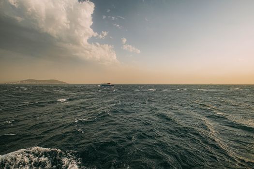 Wide shot of the ocean during sunset with a distant boat and dramatic cloud cover.
