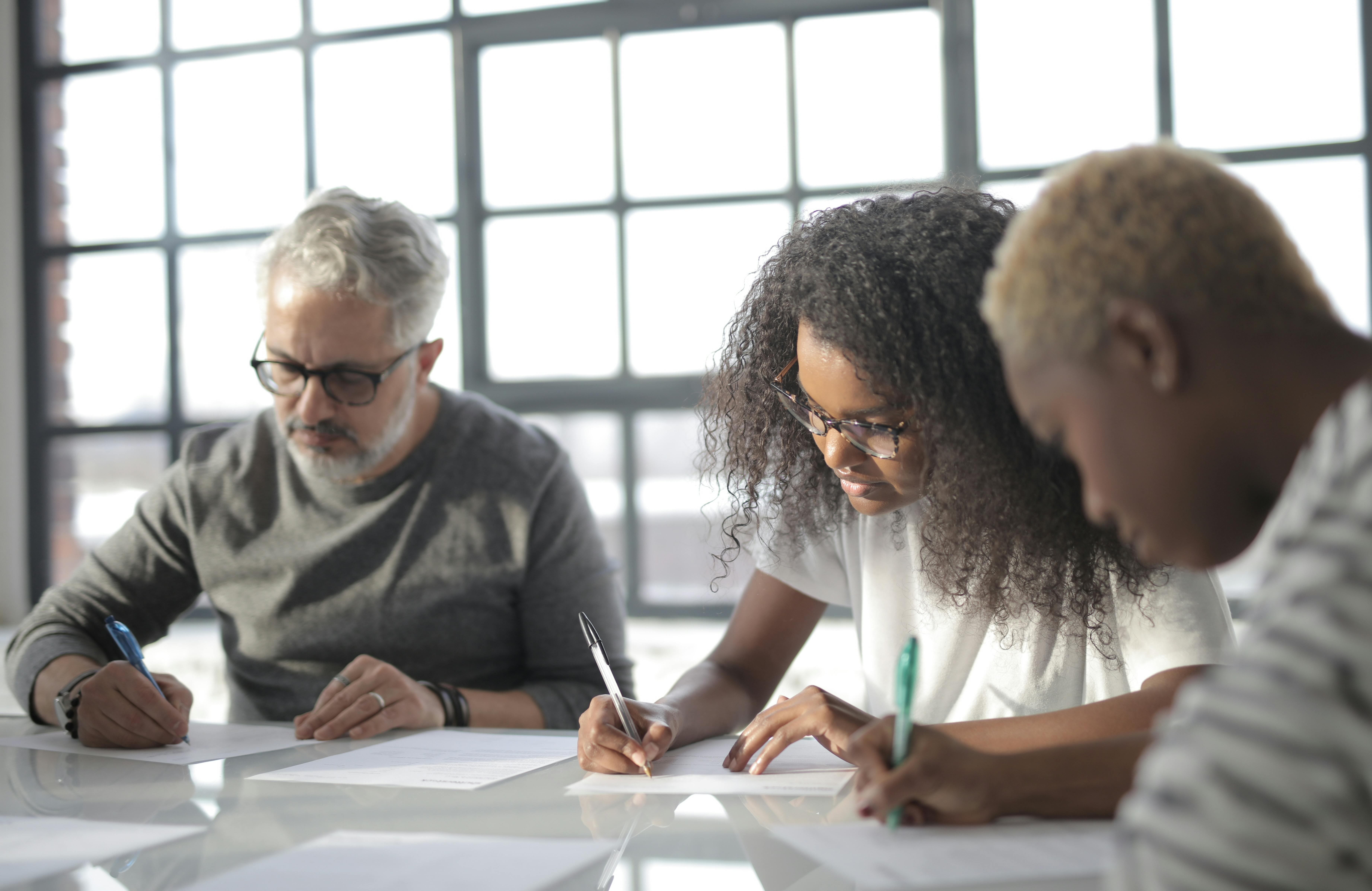 focused multiracial coworkers writing papers in office