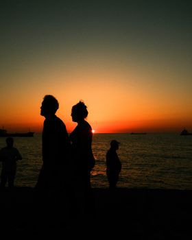 Silhouetted figures walking along a beach during a vivid sunset.