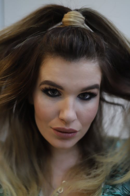 Headshot of serious female with ponytail and bright makeup looking at camera arrogantly