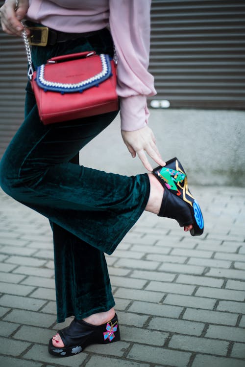 Crop stylish woman touching shoe heel on street