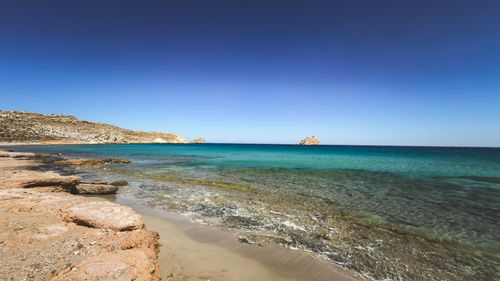 Free Tranquil beach scene with clear turquoise waters and rocky coastline under a blue sky. Stock Photo