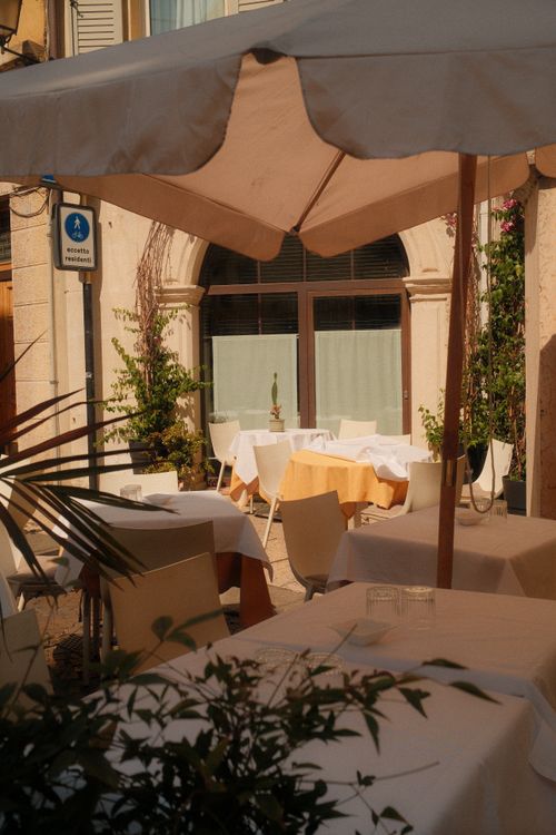 Free Sunlit outdoor cafe setting in Verona, Italy, with elegant table arrangements and umbrellas. Stock Photo