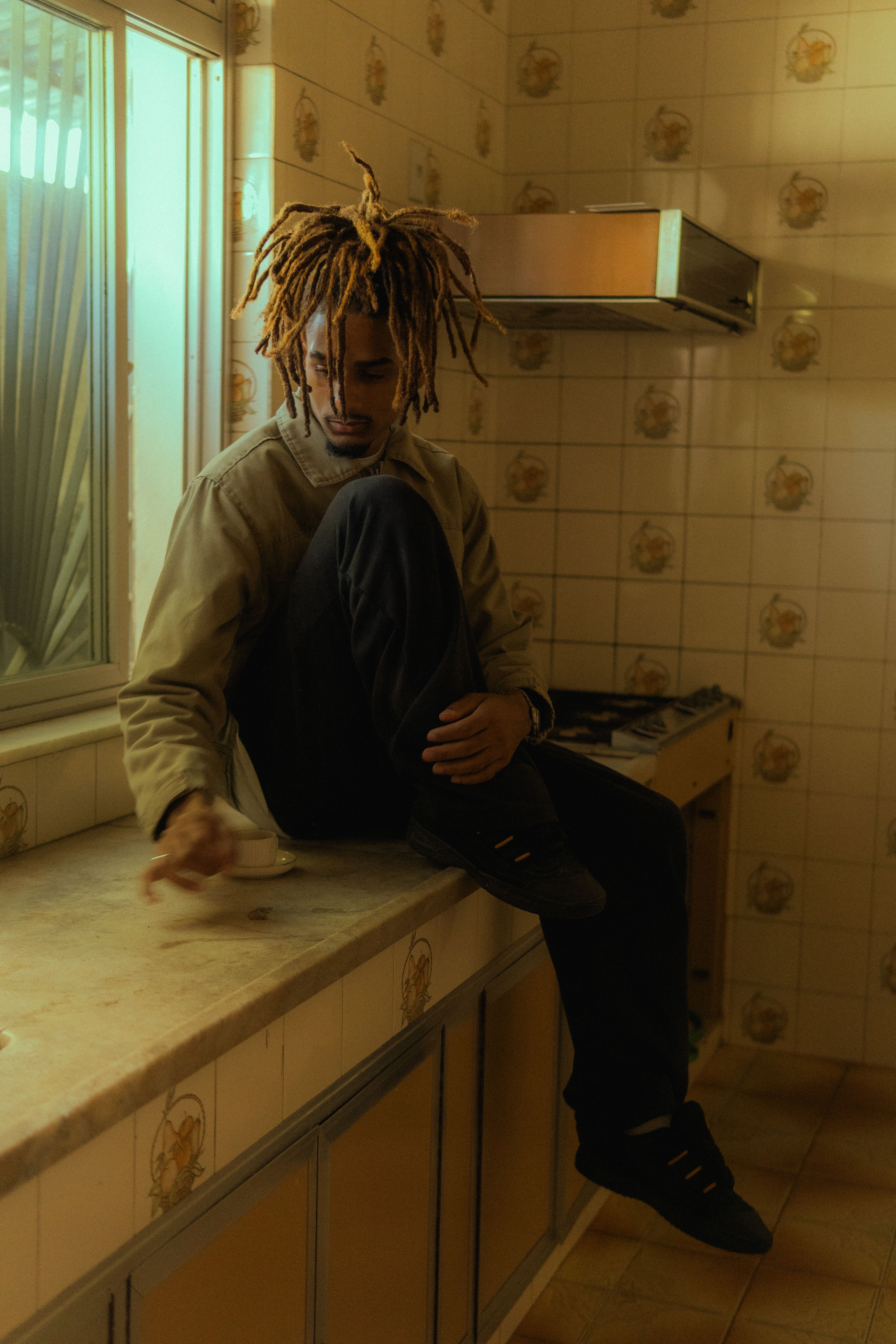 Man sits thoughtfully on a kitchen counter in a dimly lit, retro-style kitchen.