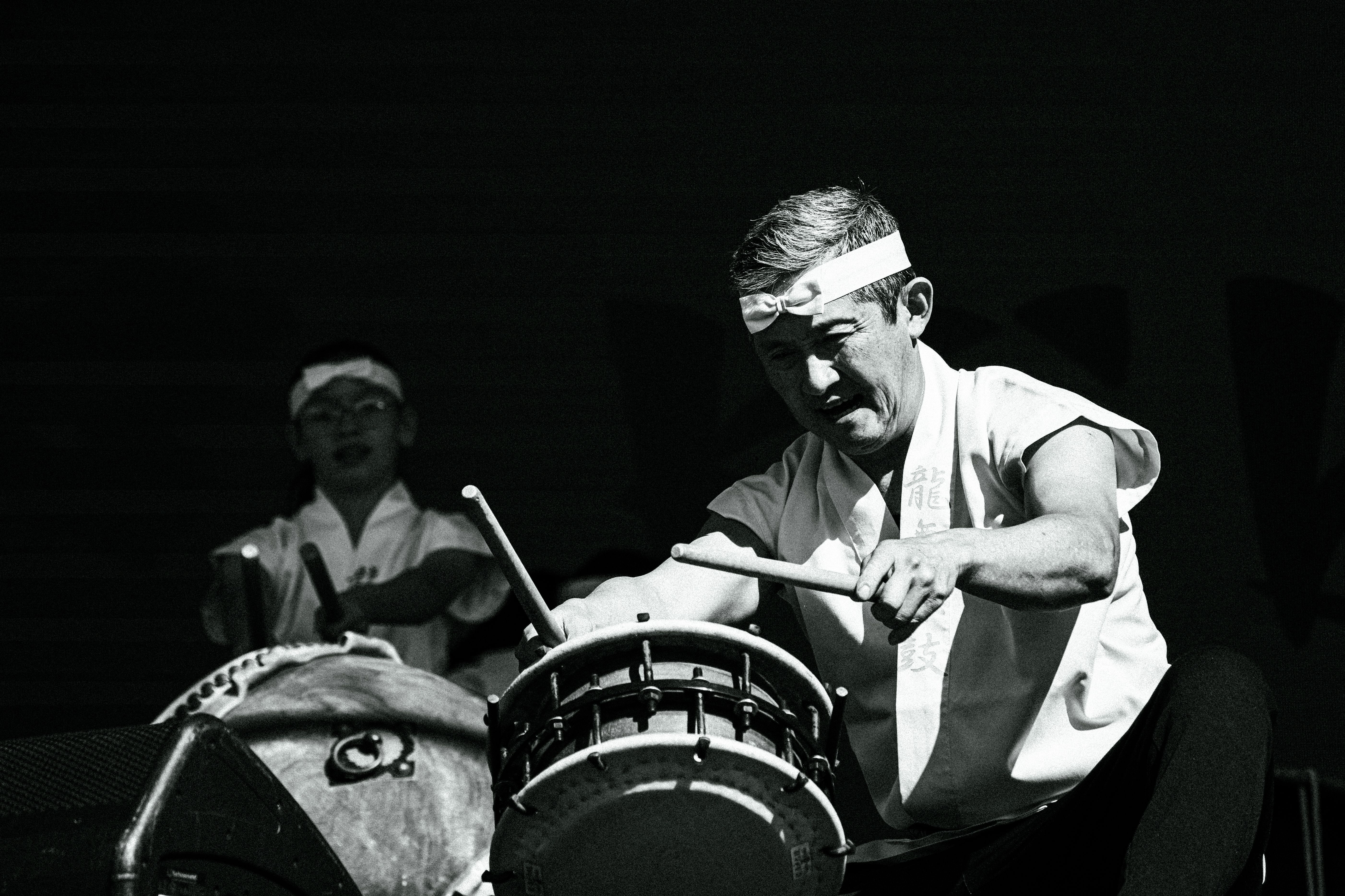Black and white photo of taiko drummers giving a powerful performance on stage.
