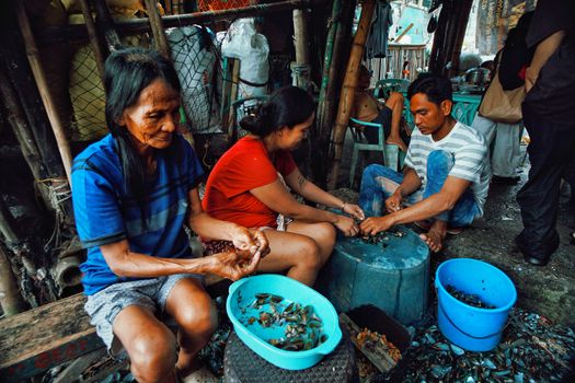 Three adults shelling mussels in a rustic indoor setting, showcasing traditional livelihood and community effort.