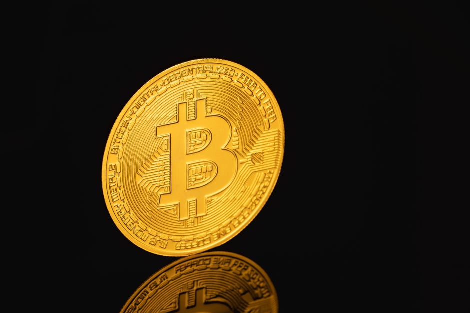 Elegante primer plano de una moneda de Bitcoin reflejándose en una superficie negra, símbolo de la moneda digital.