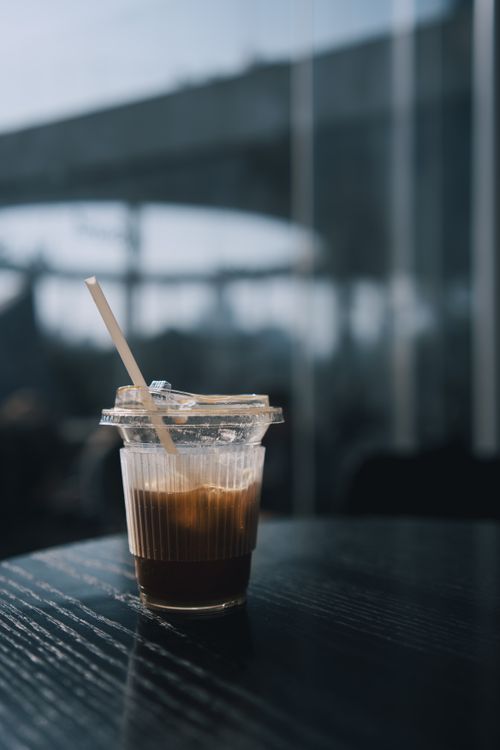 Free A single plastic cup with iced coffee and a straw on a table indoors, featuring soft lighting. Stock Photo